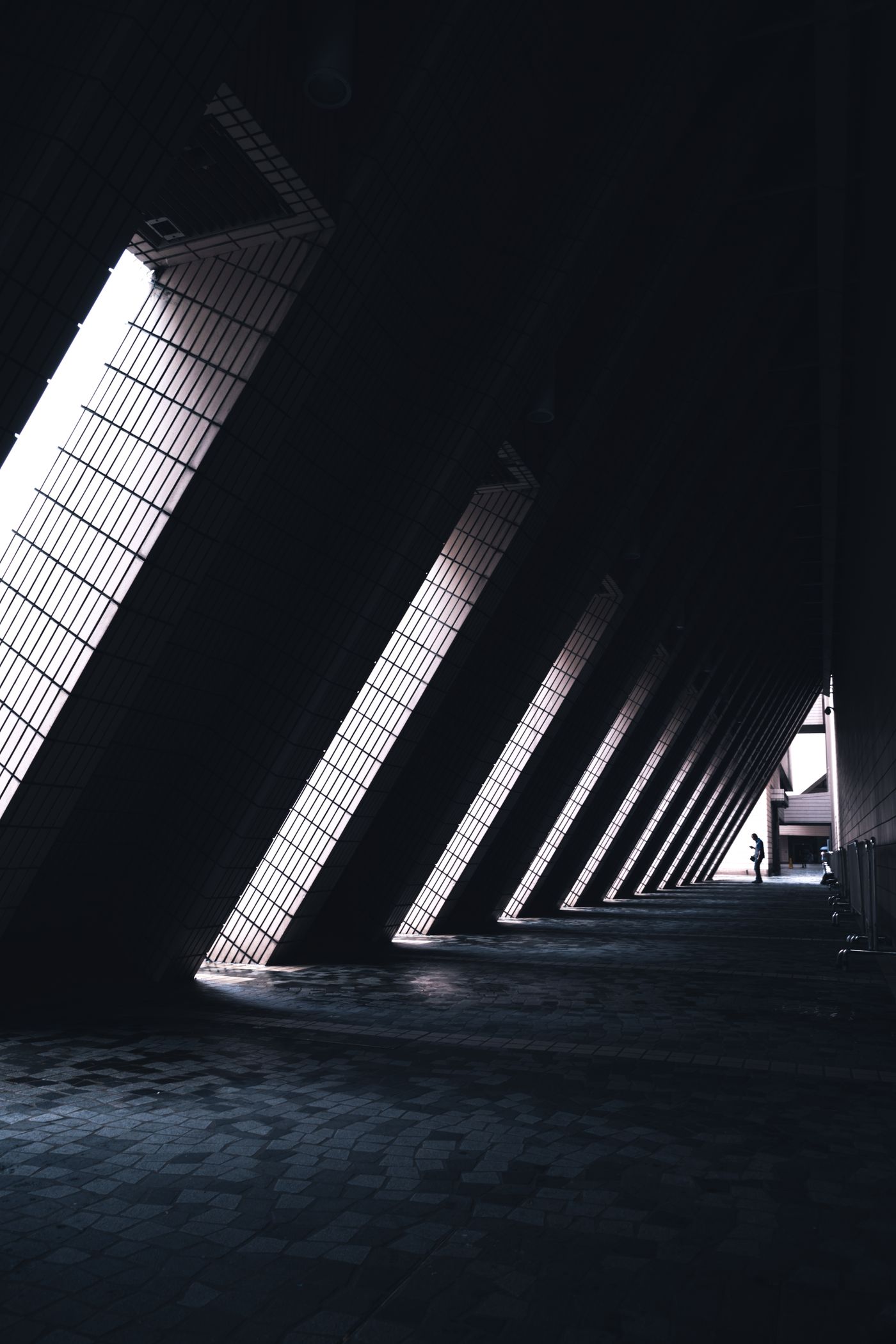 A person walking through monumental dark architecture cut by bands of daylight