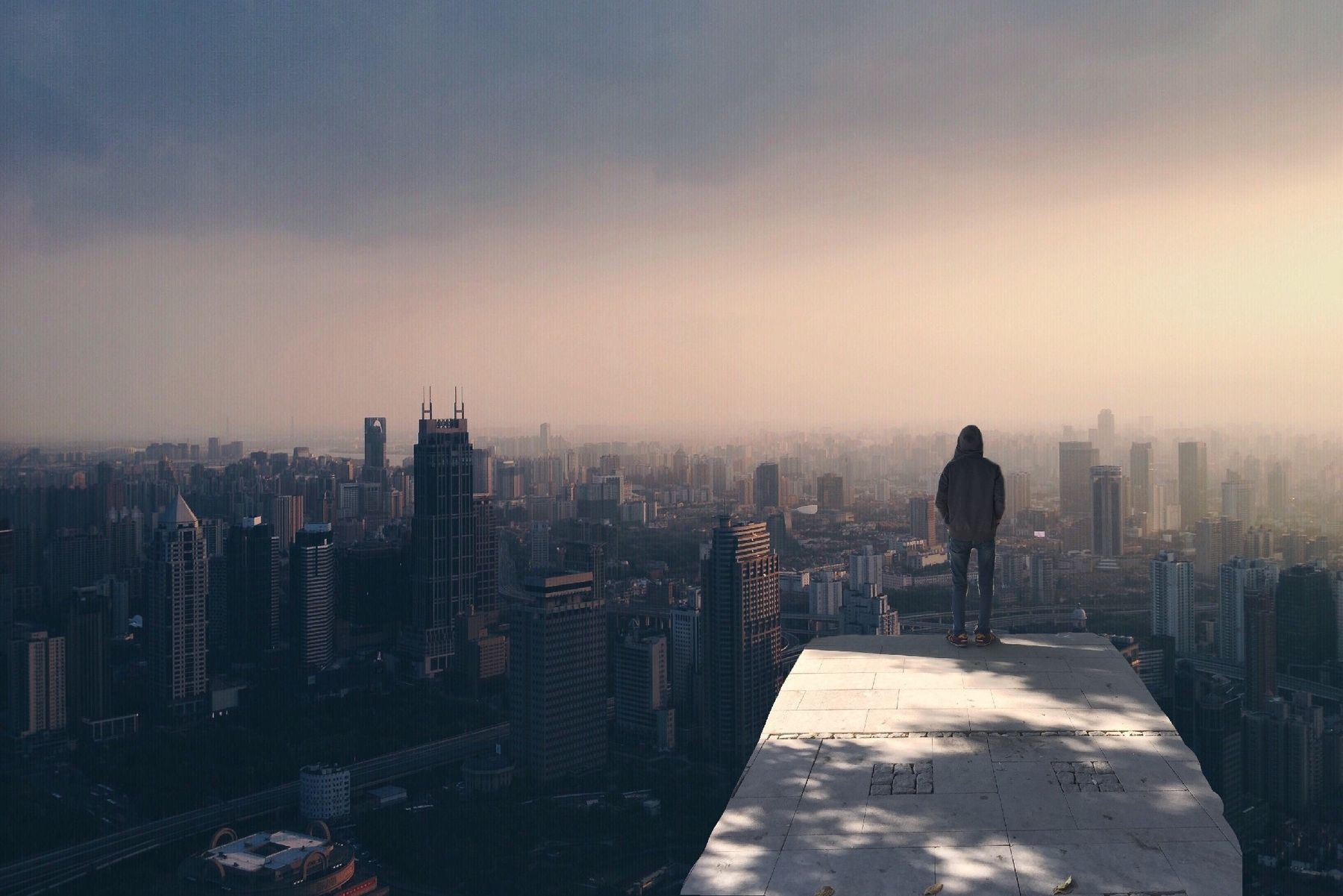 A figure standing on a rooftop, overlooking a city in morning haze